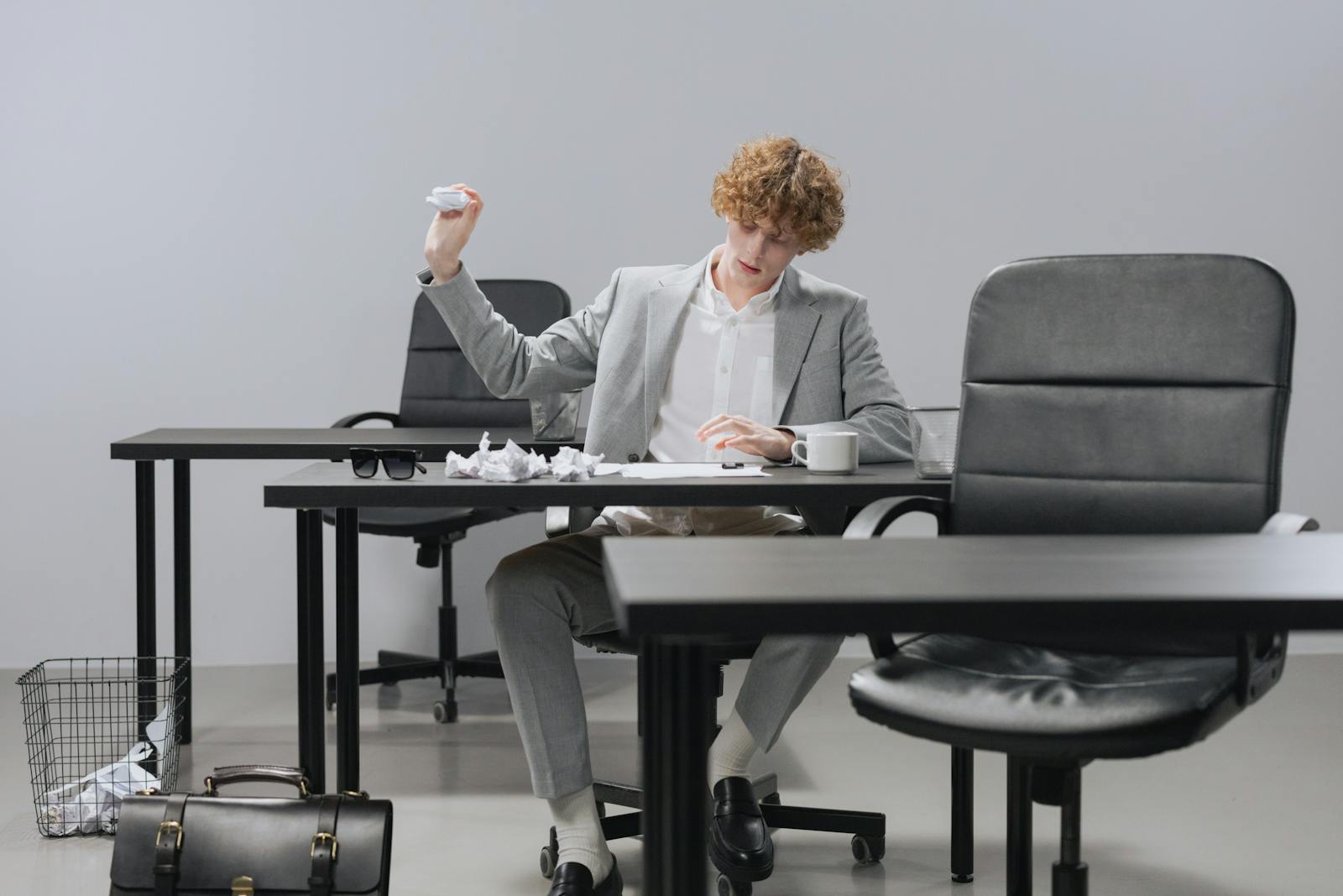 Confident young man in gray suit tossing crumpled paper in modern office setting.